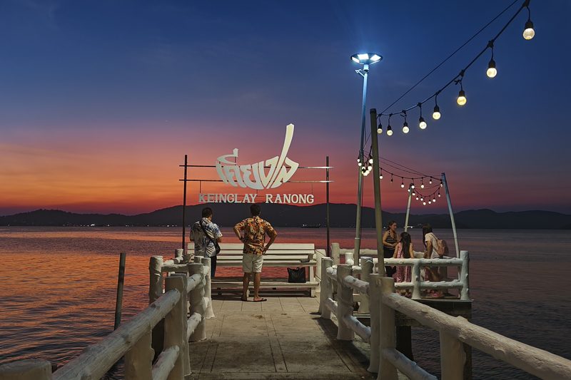 สะพานท่าเรือของร้านยื่นลงทะเลยามโพล้เพล้ ป้ายชื่อเคียงเล ไฟระย้า และภูเขาฝั่งตรงข้าม